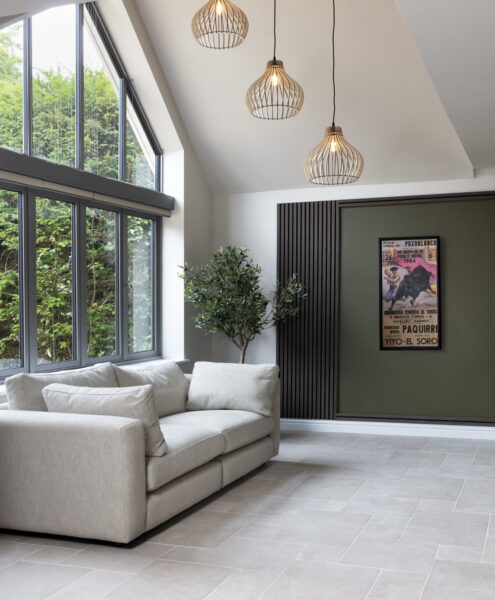 Interior design for hidden disabilities. Neutral walls, floor and sofa. Calming textures of wood paneling and wooden light shades with green accents and a plant.