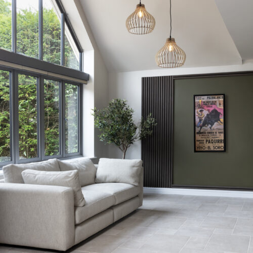 Interior design for hidden disabilities. Neutral walls, floor and sofa. Calming textures of wood paneling and wooden light shades with green accents and a plant.