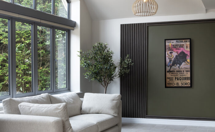 Interior design for hidden disabilities. Neutral walls, floor and sofa. Calming textures of wood paneling and wooden light shades with green accents and a plant.