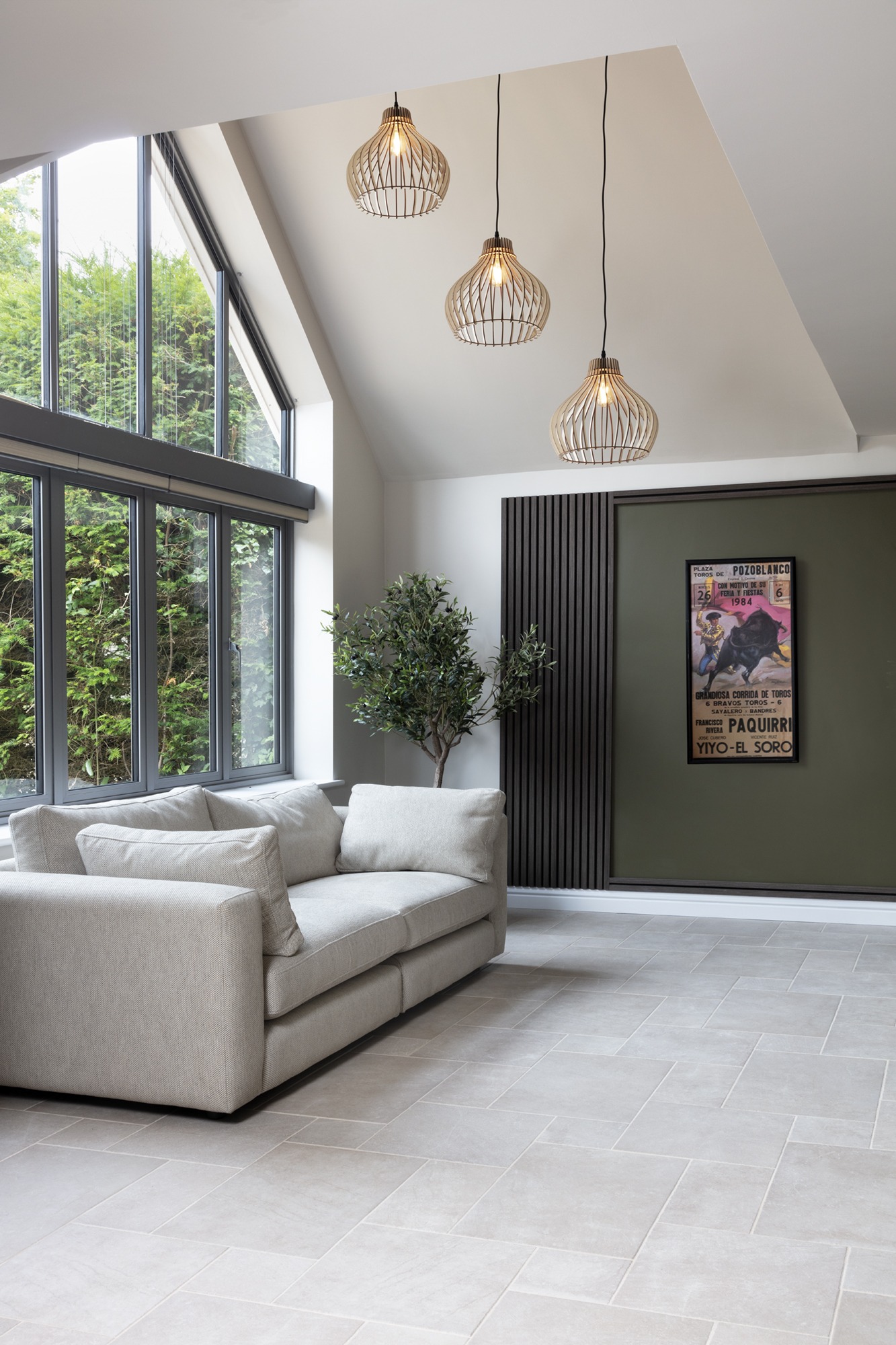 Interior design for hidden disabilities. Neutral walls, floor and sofa. Calming textures of wood paneling and wooden light shades with green accents and a plant.